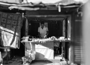 A man working at a food stall in Jeypore market, India, in black and white.