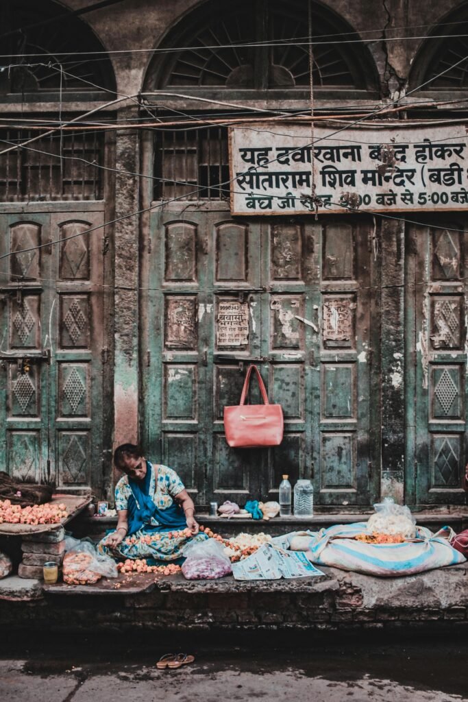 A street vendor sells flowers in front of an old building in a bustling Indian marketplace.